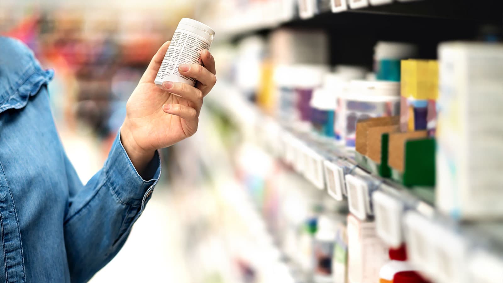 A woman holds a bottle of medicine while shopping in a store aisle in front of ESLs (electronic shelf labels)